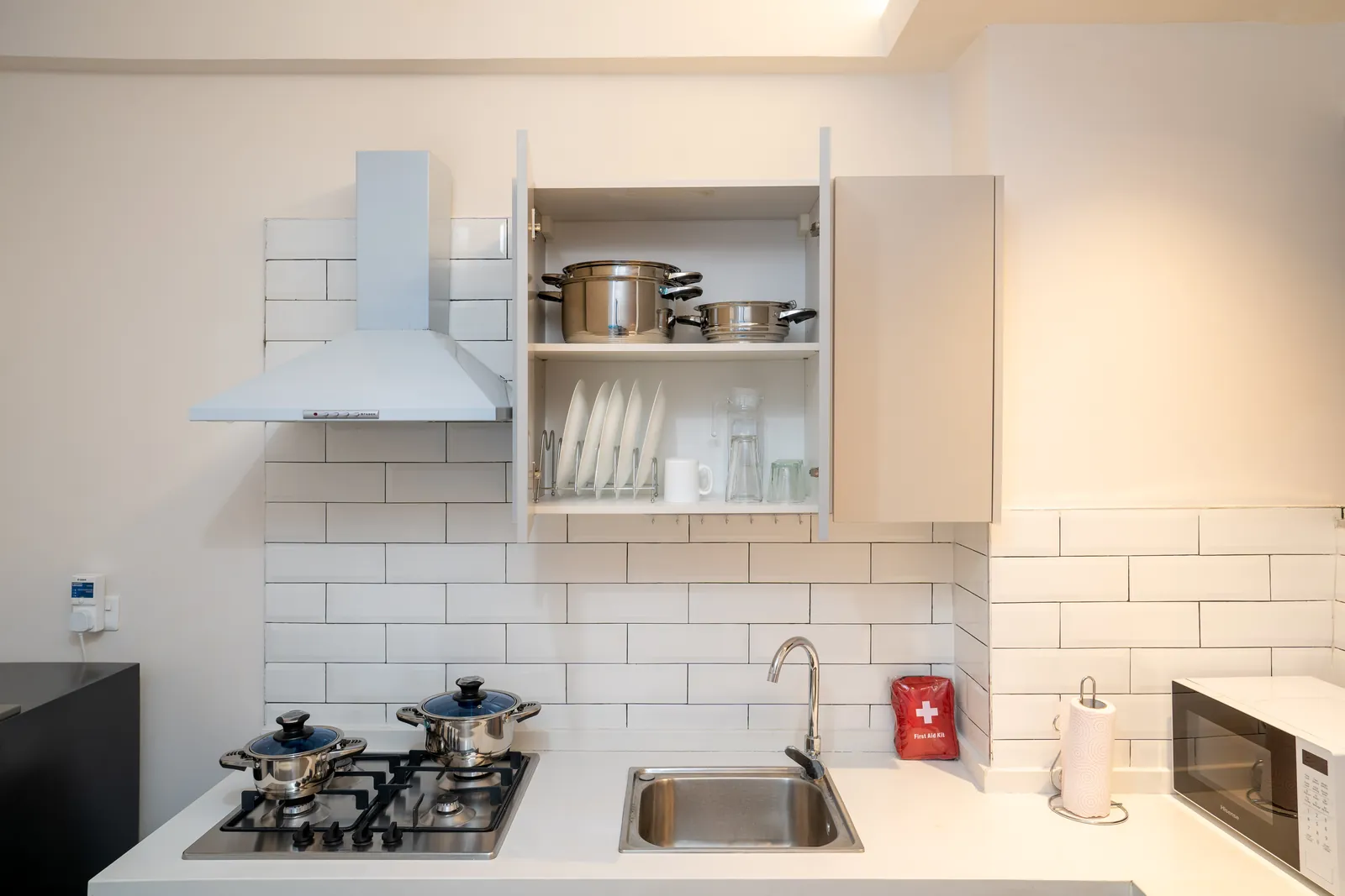 Kitchen cupboards with cookware, plates, mugs and glasses above the hob and sink