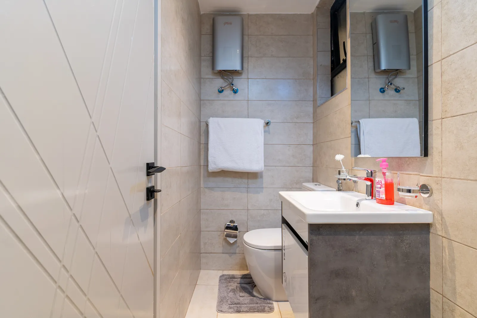 Tiled bathroom with a vanity sink, mirror, white towels and water heater